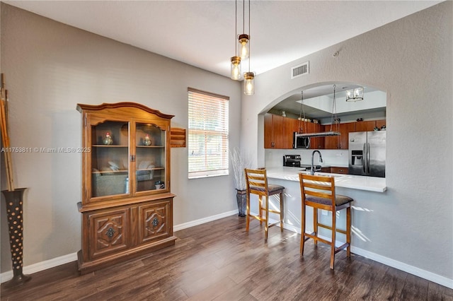 kitchen featuring arched walkways, stainless steel appliances, visible vents, dark wood-type flooring, and a kitchen breakfast bar