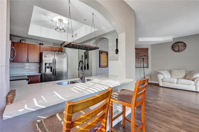 kitchen with arched walkways, wood finished floors, a sink, stainless steel refrigerator with ice dispenser, and a raised ceiling