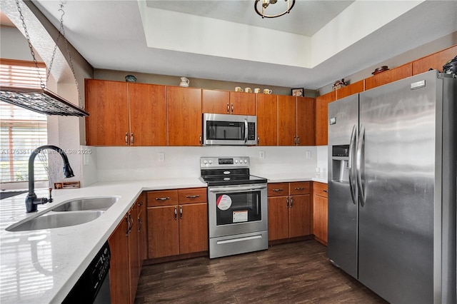 kitchen with a sink, light countertops, appliances with stainless steel finishes, a tray ceiling, and brown cabinetry