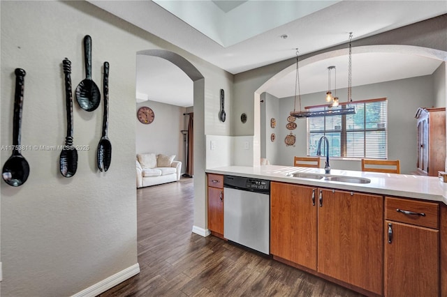 kitchen with brown cabinets, dark wood-style flooring, light countertops, stainless steel dishwasher, and a sink