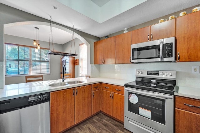 kitchen featuring brown cabinetry, appliances with stainless steel finishes, dark wood-type flooring, light countertops, and a sink