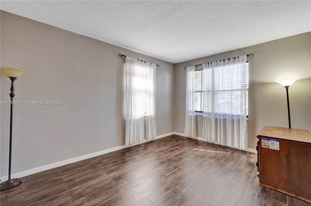 spare room featuring dark wood-type flooring, a textured ceiling, and baseboards