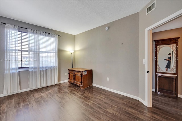 unfurnished room featuring baseboards, a textured ceiling, visible vents, and dark wood-type flooring