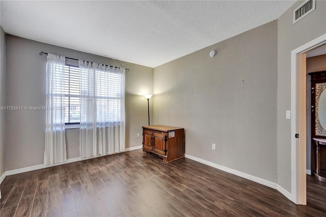 spare room with dark wood-type flooring, visible vents, a textured ceiling, and baseboards