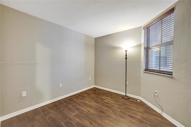 empty room featuring a textured wall, wood finished floors, and baseboards