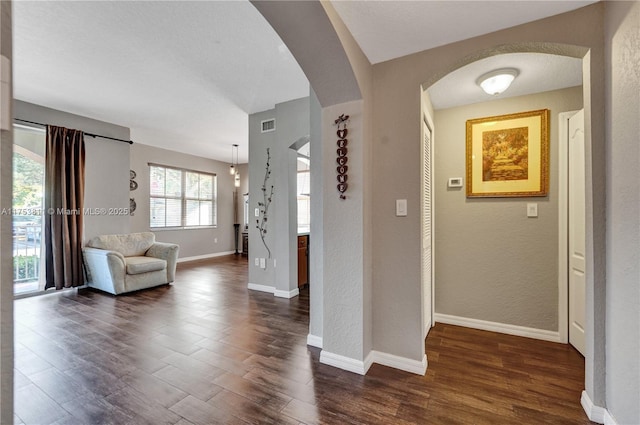 entryway featuring arched walkways, dark wood-style flooring, visible vents, a textured wall, and baseboards