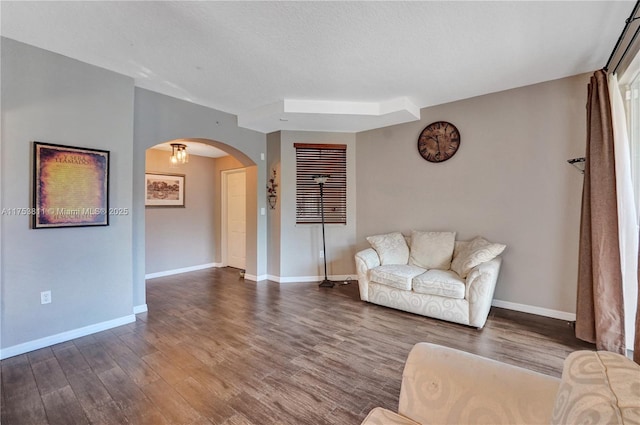 unfurnished living room with baseboards, a textured ceiling, arched walkways, and wood finished floors