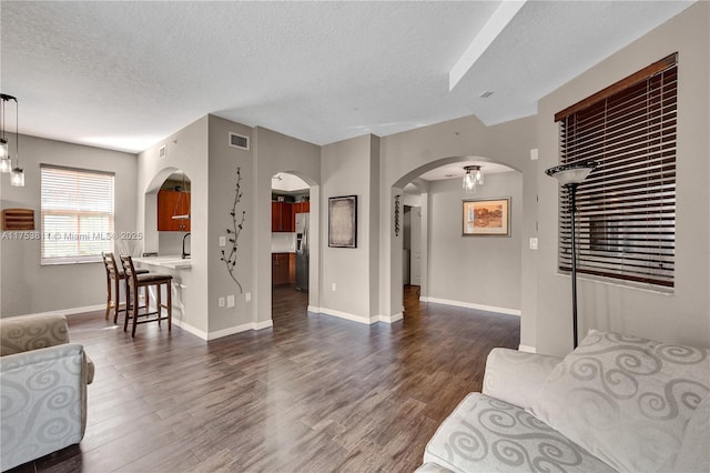 living room with a textured ceiling, visible vents, arched walkways, and dark wood-type flooring