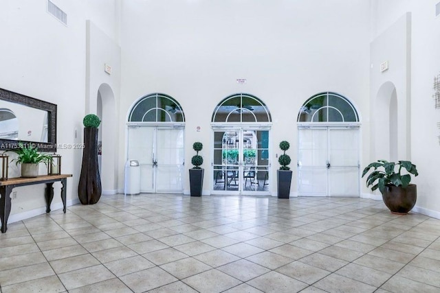 entrance foyer with light tile patterned floors, visible vents, a high ceiling, and baseboards