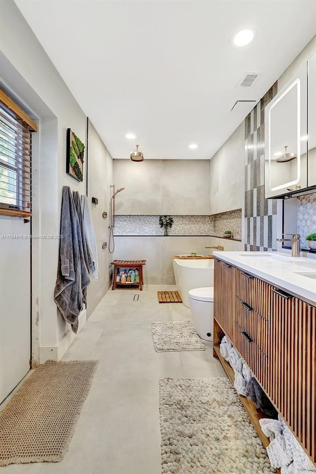 bathroom featuring toilet, recessed lighting, visible vents, a freestanding bath, and double vanity