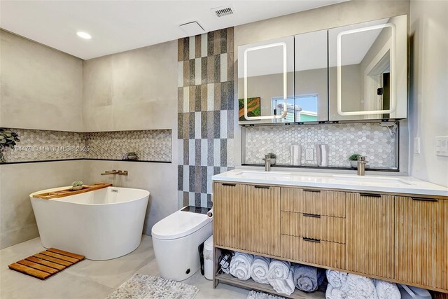 bathroom with toilet, visible vents, tile walls, a freestanding bath, and double vanity