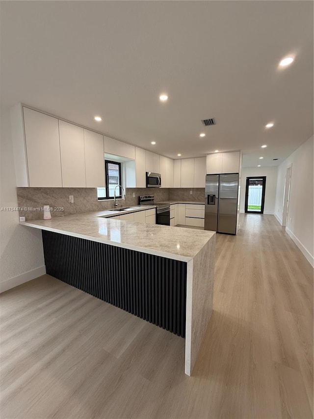 kitchen with stainless steel appliances, a peninsula, light wood-style flooring, and decorative backsplash