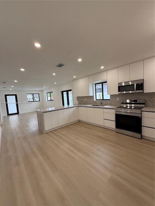 kitchen featuring light wood-style flooring, appliances with stainless steel finishes, white cabinetry, a sink, and modern cabinets