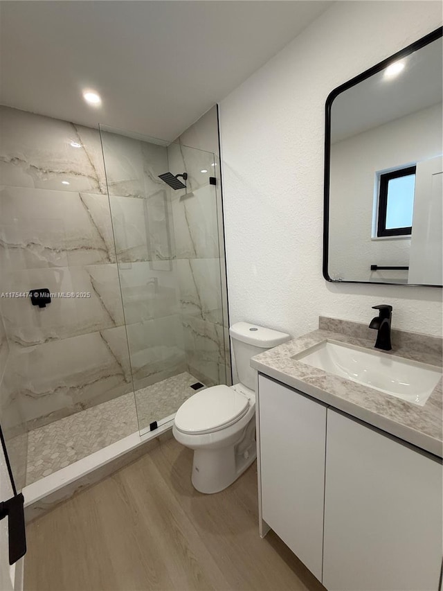 bathroom featuring toilet, a marble finish shower, wood finished floors, and vanity