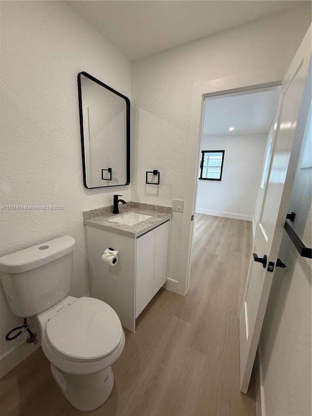 half bath featuring baseboards, a textured wall, toilet, wood finished floors, and vanity