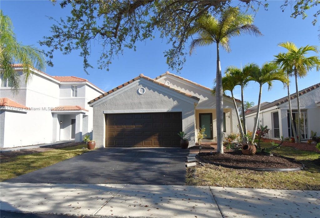 view of front of house with a garage, a tiled roof, aphalt driveway, and stucco siding