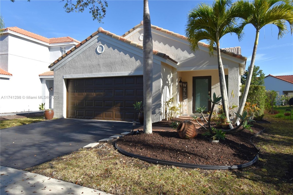 mediterranean / spanish-style house with a garage, driveway, a tiled roof, and stucco siding