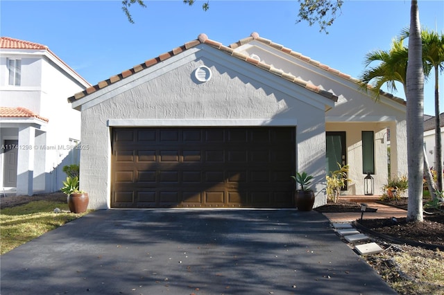 mediterranean / spanish-style home with a garage, a tiled roof, aphalt driveway, and stucco siding