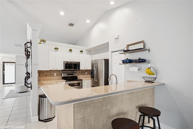 kitchen with backsplash, a peninsula, appliances with stainless steel finishes, light tile patterned flooring, and light countertops