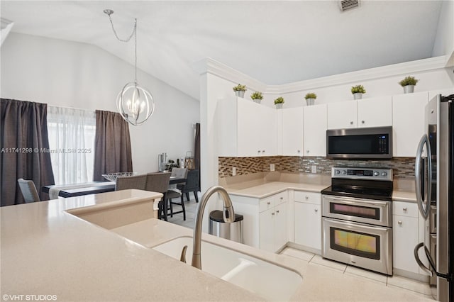 kitchen with a chandelier, lofted ceiling, appliances with stainless steel finishes, white cabinetry, and a sink