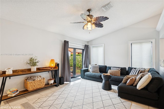living area featuring visible vents, vaulted ceiling, light tile patterned floors, a textured ceiling, and a ceiling fan