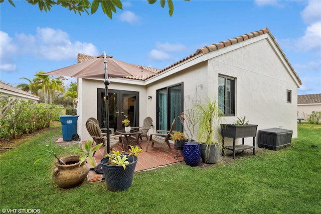 back of property with stucco siding, a patio, a lawn, and a tile roof