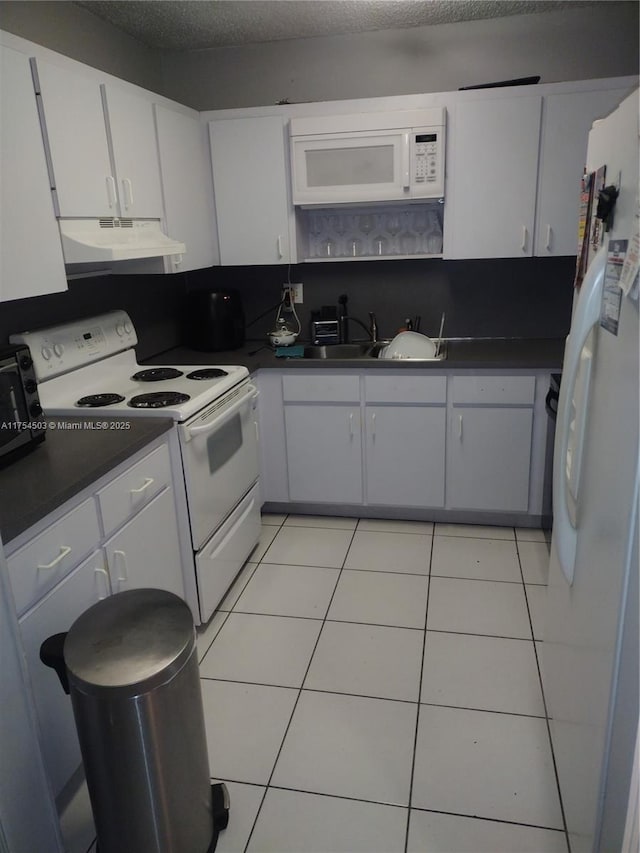 kitchen featuring light tile patterned floors, dark countertops, a sink, white appliances, and under cabinet range hood