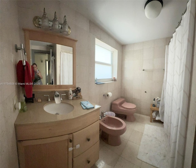 bathroom with tile walls, toilet, a bidet, vanity, and tile patterned flooring