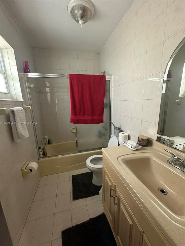 bathroom featuring enclosed tub / shower combo, tile patterned flooring, toilet, vanity, and tile walls