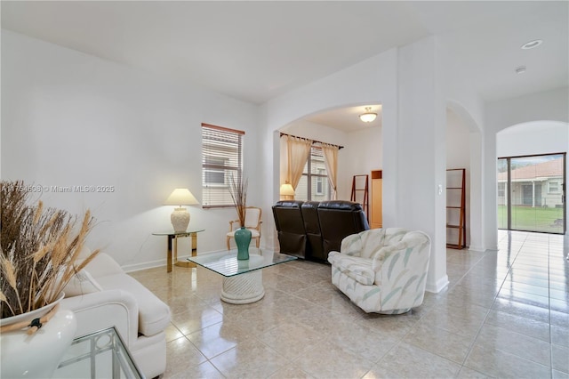 living area featuring arched walkways, light tile patterned flooring, and baseboards