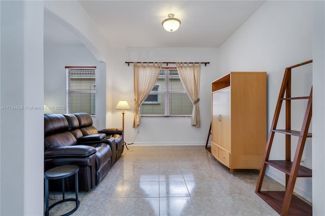 living area with light tile patterned floors, arched walkways, a wealth of natural light, and baseboards