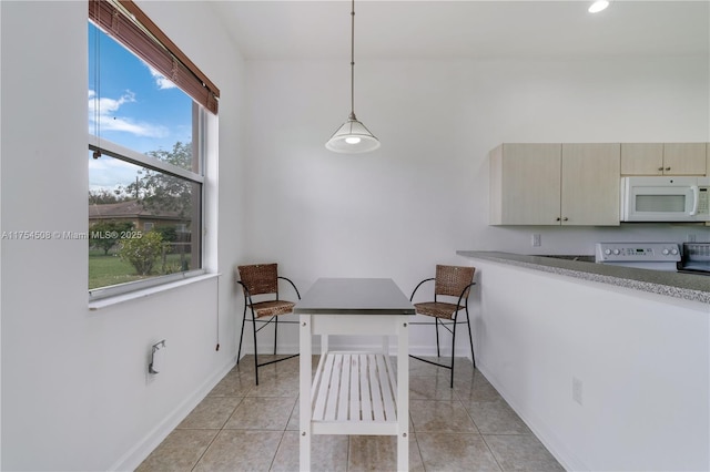 kitchen featuring light tile patterned floors, baseboards, white microwave, stove, and decorative light fixtures