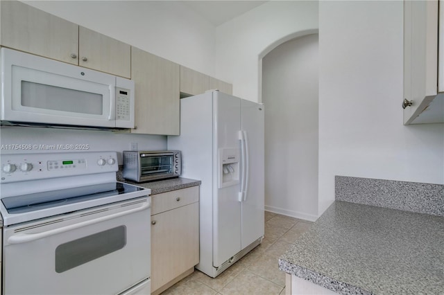 kitchen with arched walkways, white appliances, a toaster, and light tile patterned floors