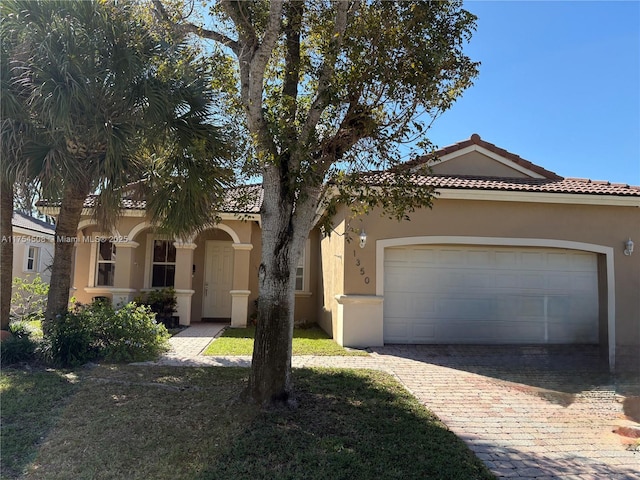 mediterranean / spanish-style house with decorative driveway, an attached garage, a tile roof, and stucco siding