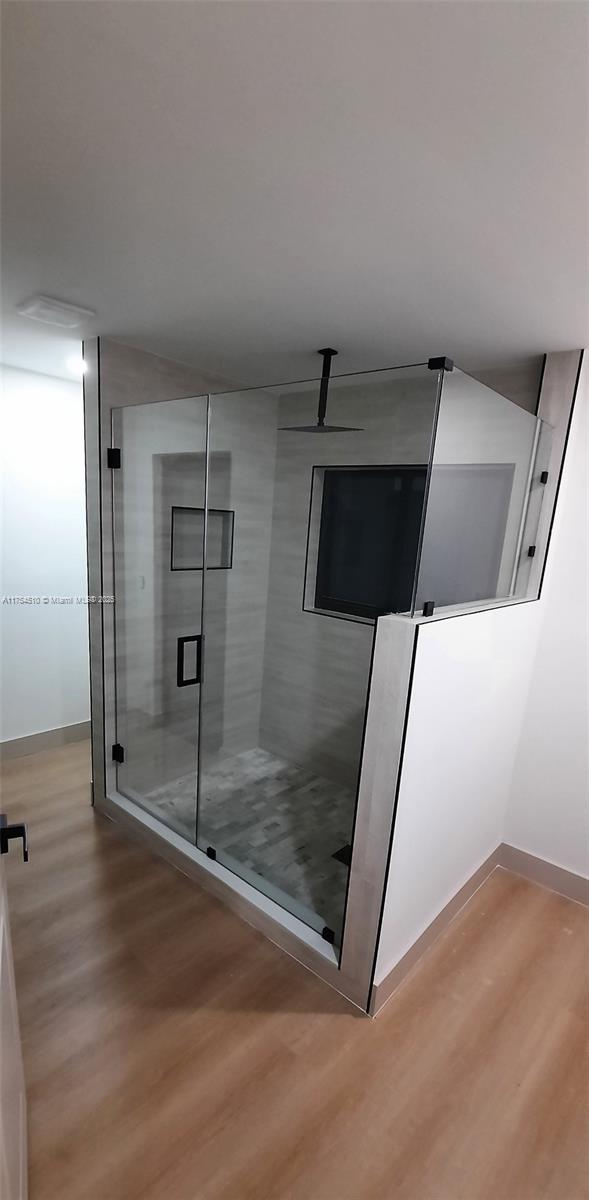 full bathroom featuring a stall shower, baseboards, and wood finished floors