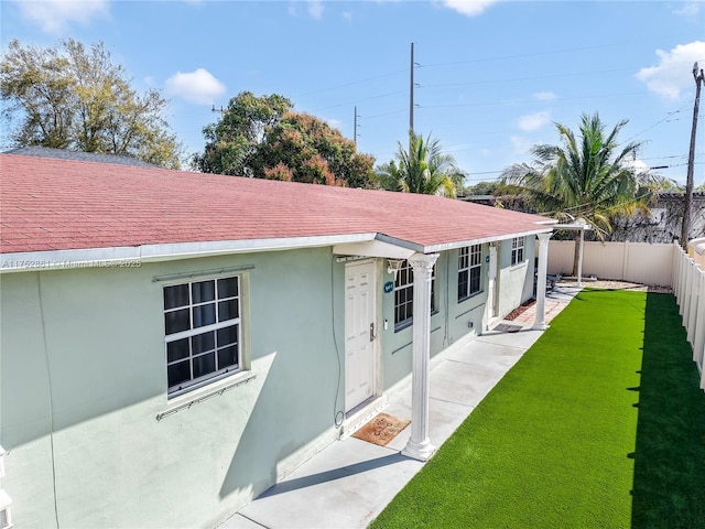 rear view of house with a yard, a shingled roof, a fenced backyard, and stucco siding