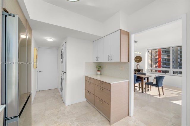 kitchen with tasteful backsplash, white cabinets, stacked washer and clothes dryer, freestanding refrigerator, and light countertops