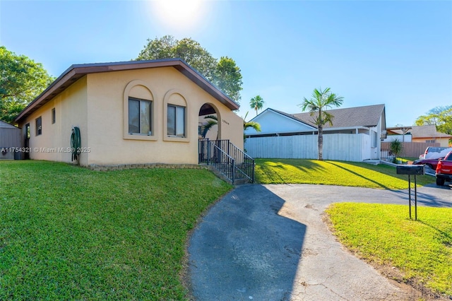 view of front of home with fence, driveway, a front lawn, and stucco siding