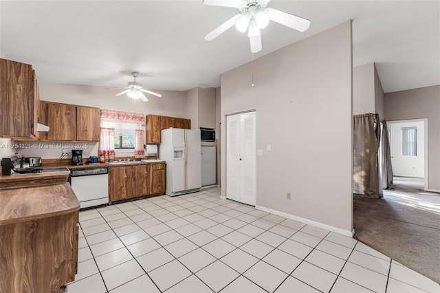 kitchen featuring white appliances, brown cabinetry, a ceiling fan, light colored carpet, and lofted ceiling