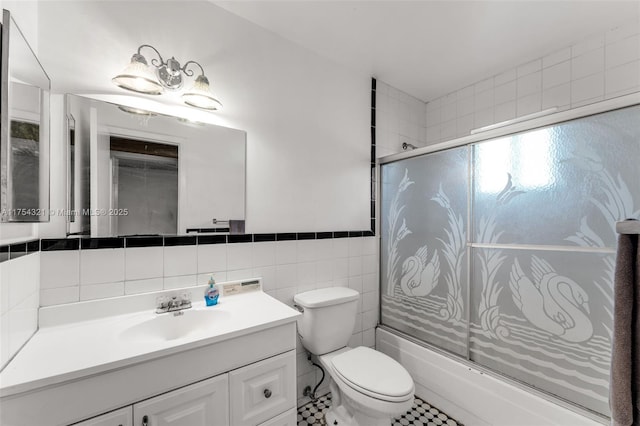 full bath featuring toilet, a wainscoted wall, combined bath / shower with glass door, vanity, and tile walls