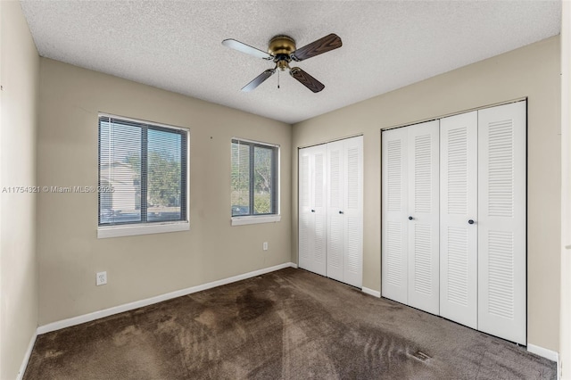 unfurnished bedroom with dark carpet, a textured ceiling, baseboards, and two closets