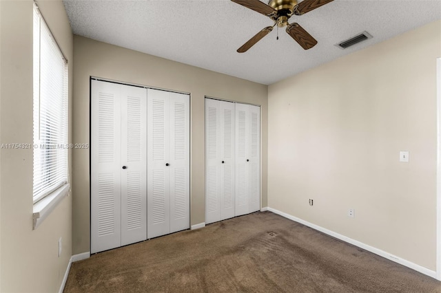 unfurnished bedroom with a textured ceiling, carpet flooring, two closets, and visible vents