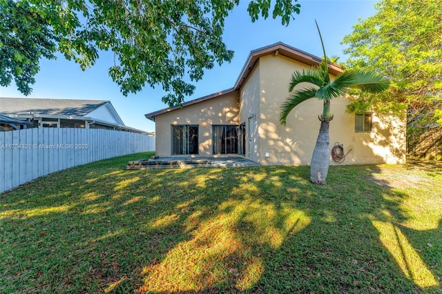 rear view of house featuring a yard, fence, and stucco siding