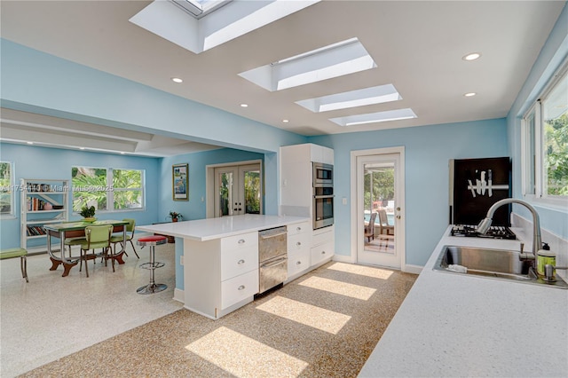 kitchen featuring french doors, light countertops, white cabinets, a sink, and a peninsula