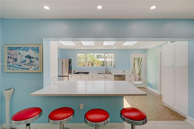 kitchen featuring a breakfast bar, appliances with stainless steel finishes, white cabinetry, a sink, and a peninsula