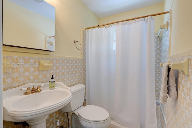 bathroom with tile walls, toilet, a wainscoted wall, a shower with curtain, and a sink