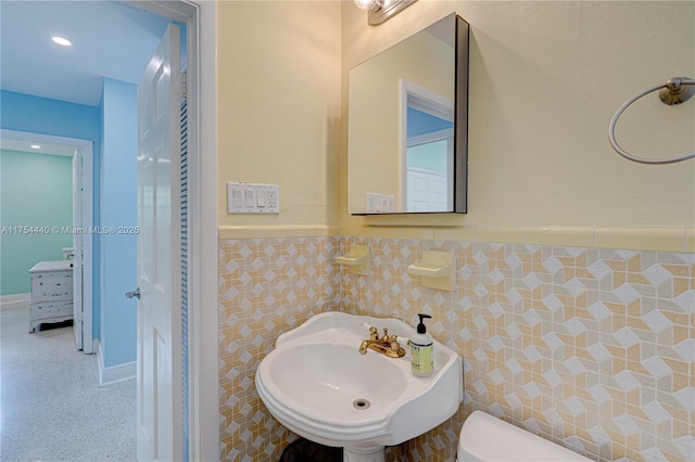 half bath with wainscoting, toilet, a sink, speckled floor, and tile walls