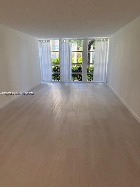 unfurnished room featuring expansive windows, baseboards, and light wood-style floors