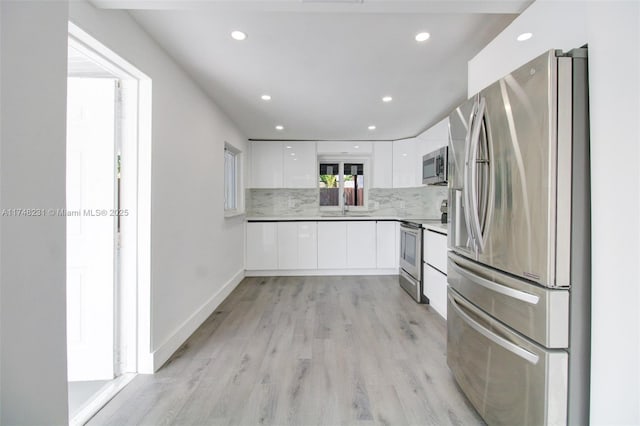 kitchen featuring white cabinets, modern cabinets, a sink, stainless steel appliances, and backsplash