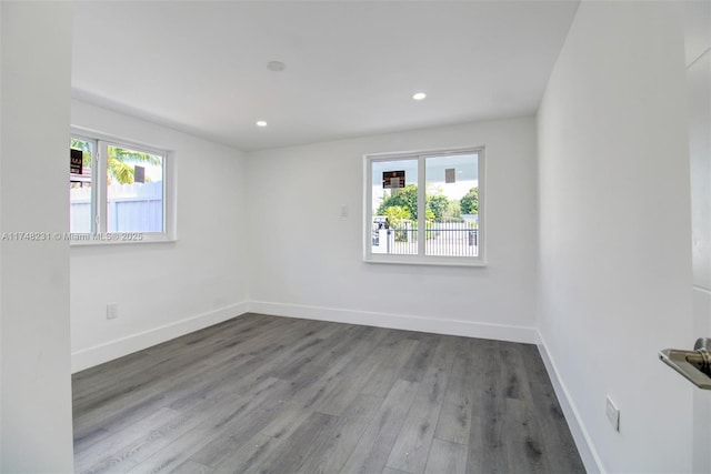 empty room with a healthy amount of sunlight, baseboards, wood finished floors, and recessed lighting